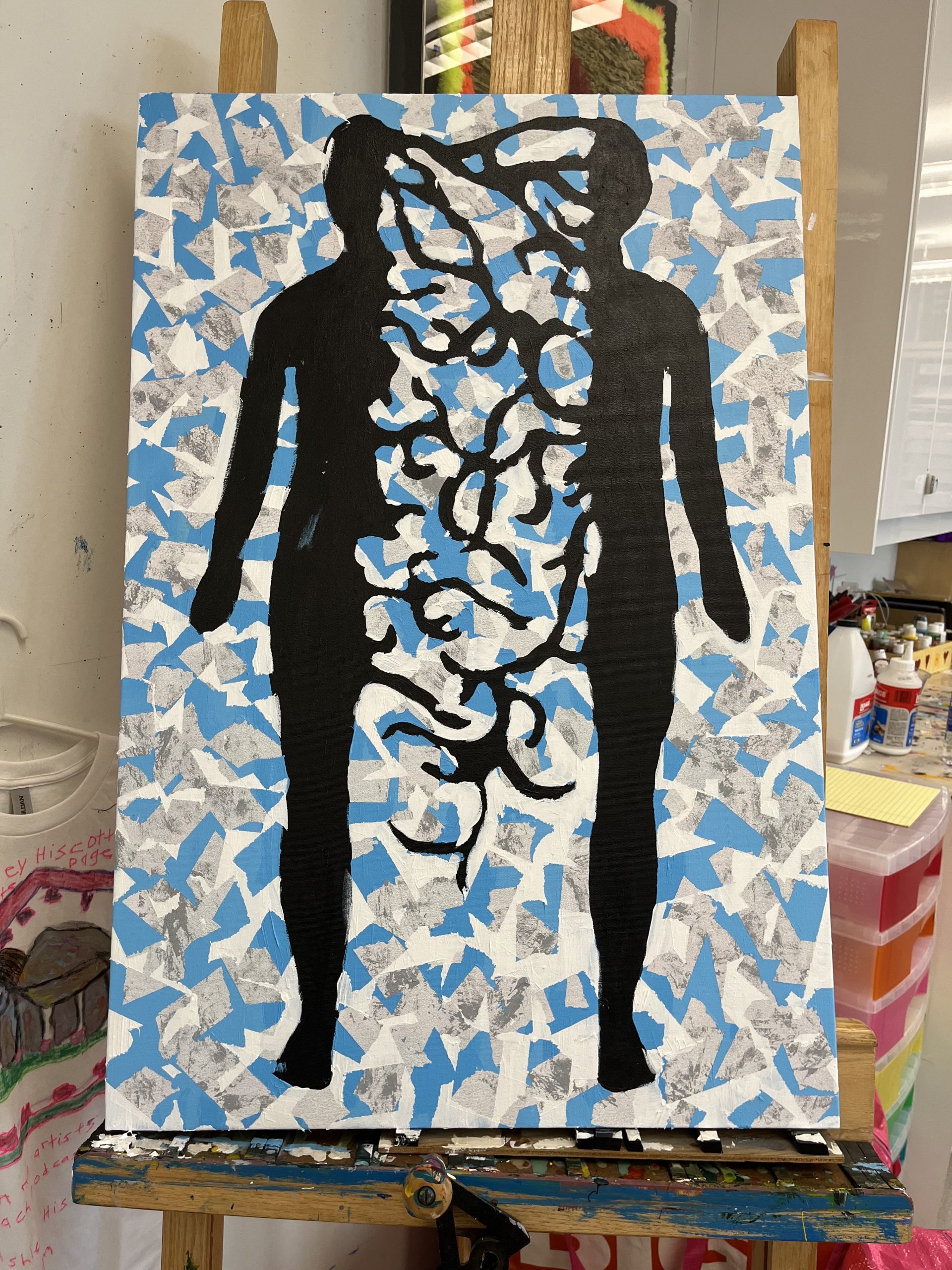 A picture of a split body, the 2 black sides show half a head, an arm and body and in between, black lines between the separated torso pieces. The background is a combination of white, blue and grey with a marble in light and dark greys with torn tape and paper placed on it in random spots to create layers.