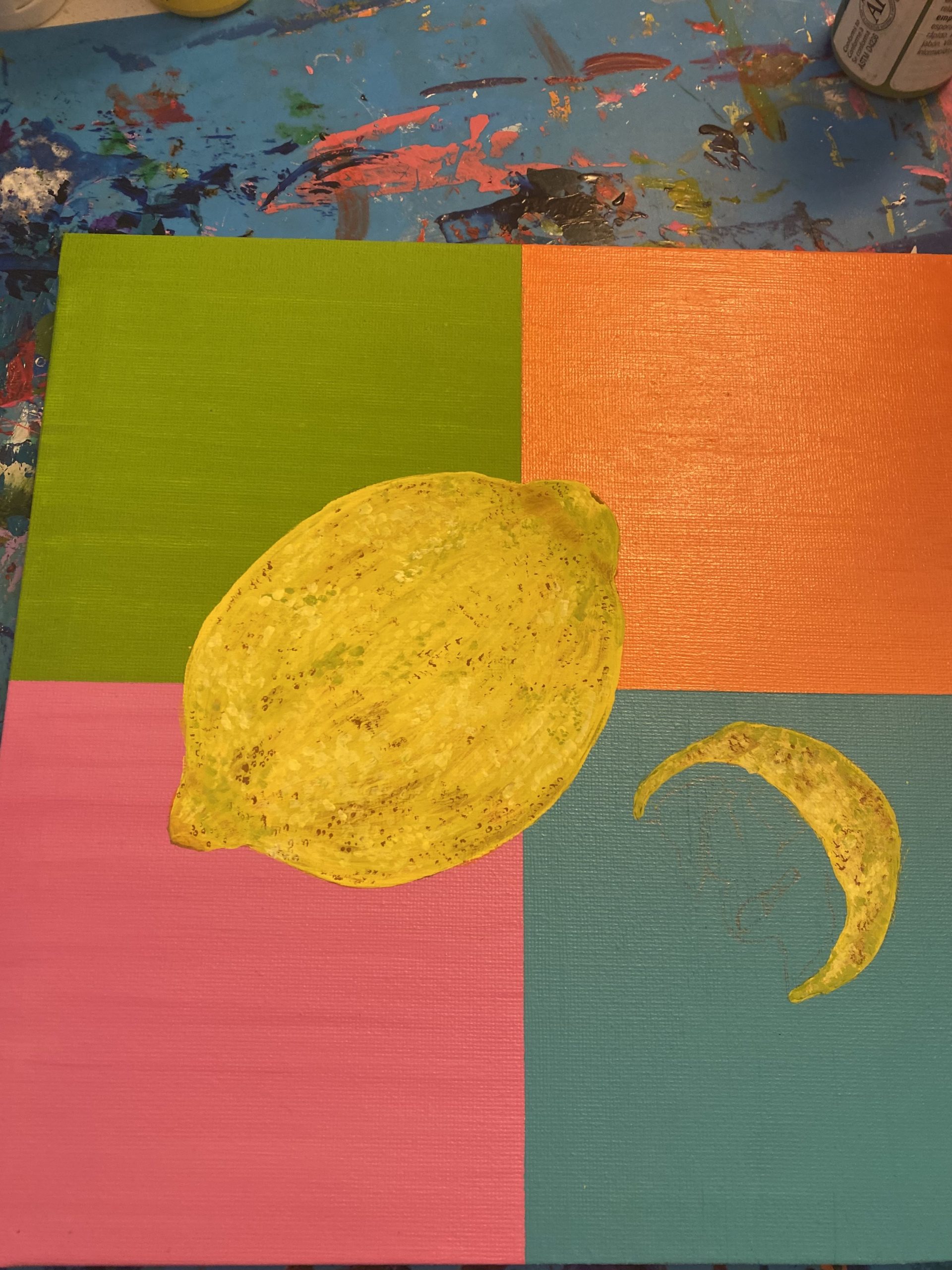 A rectangular canvas divided into four sections: the top left painted green, the bottom left painted pink, the top right painted orange, the bottom right painted blue. On top, a yellow lemon and a yellow crescent-shaped lemon slice are painted.