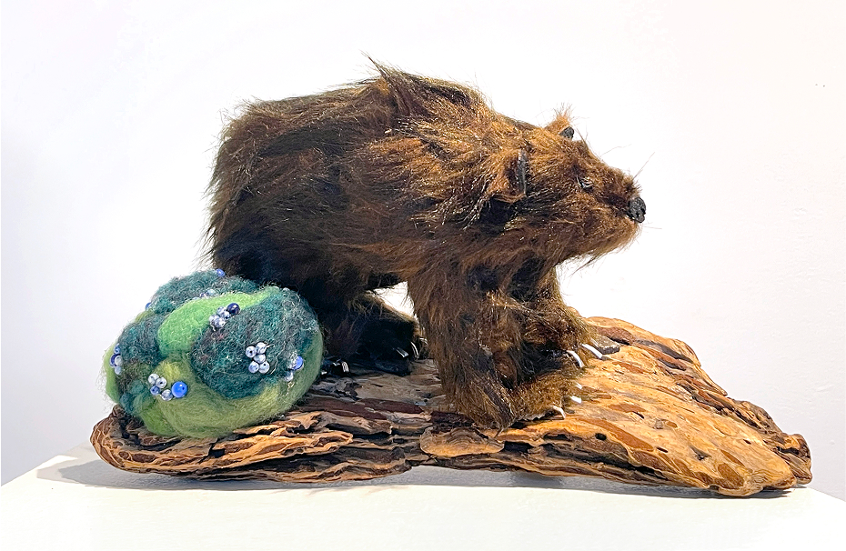 A diorama of a big grizzly bear with brown fake fur with brown beads [for eyes], black nose and then light silver claws. Light green and dark green combo needle-felted bush and then it's on a piece of wood, wood base.
