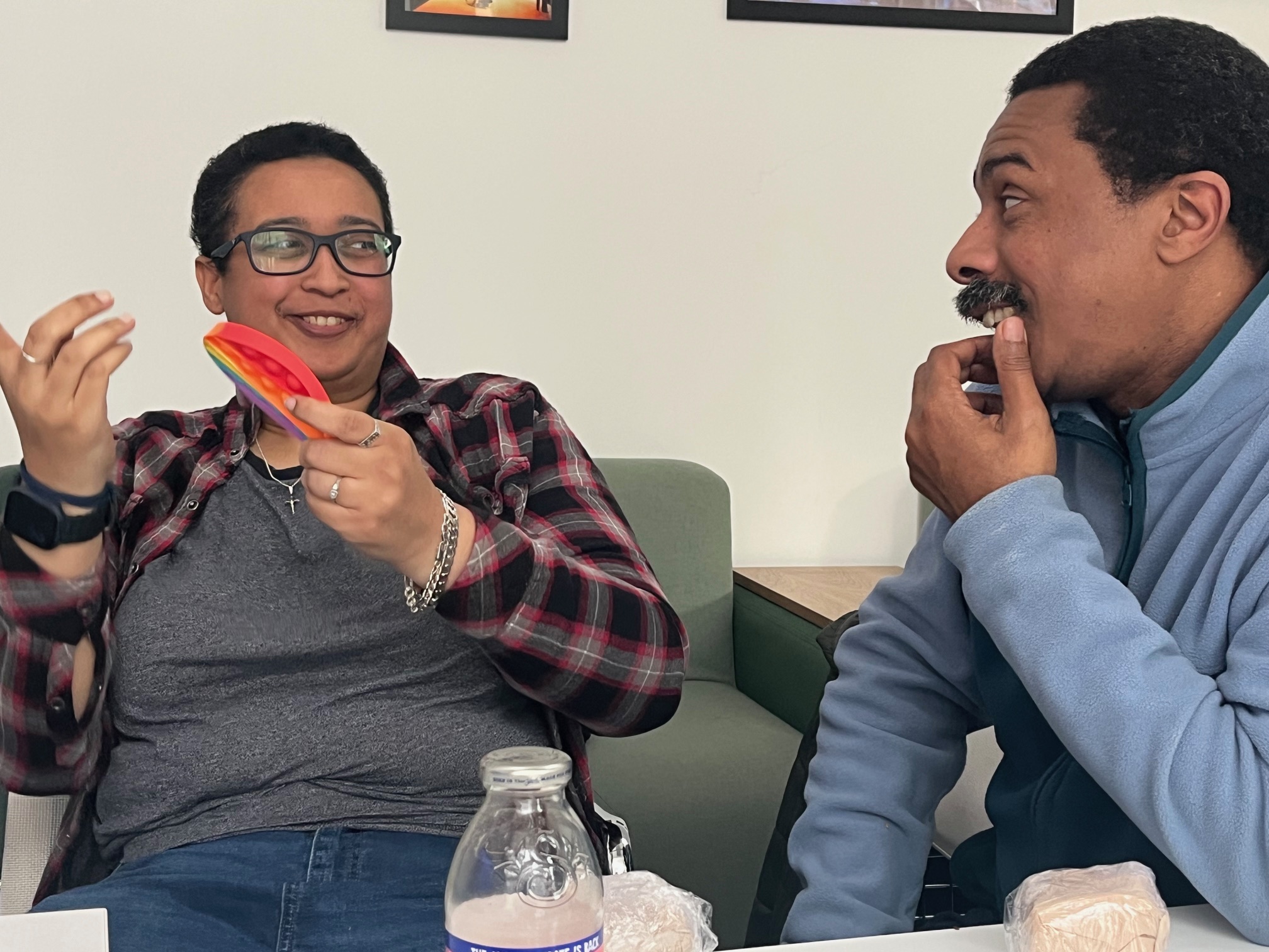 A black woman with short hair smiles, holding what looks like some watermelon. Her name is Charlene and she is meeting Thompson Hall for the first time in a Sync Shorts get together