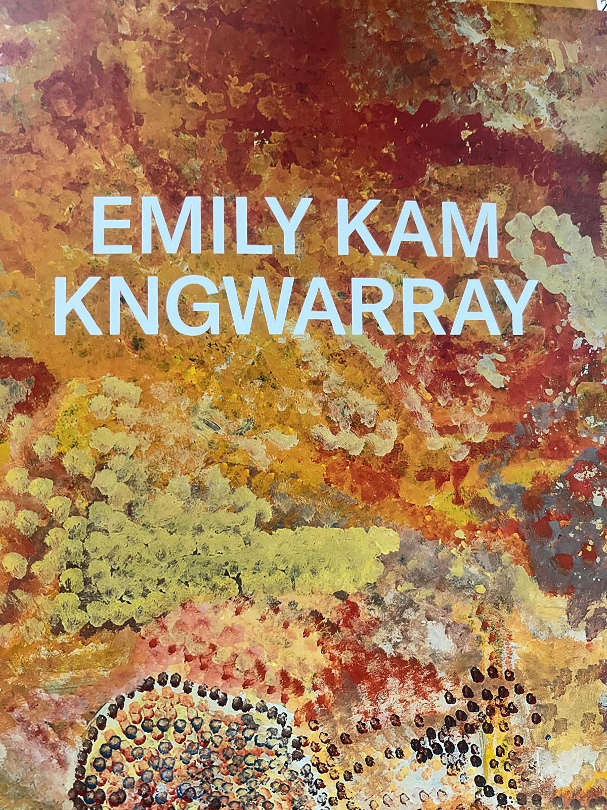 White text in capitals spell out the name EMILY KAM KNGWARRAY horizontally in line just above the middle of the images. In the background is a painting made of lines of bigger and smaller yellow, brown, white, cream and black dots.