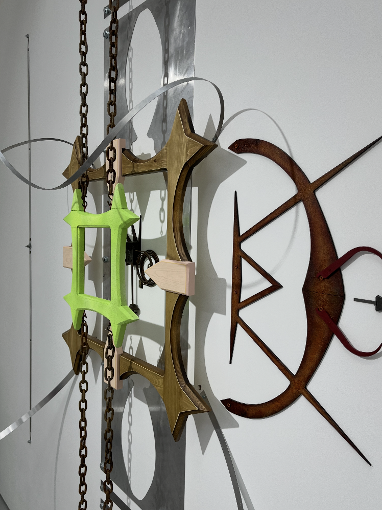 This image shows Maddi's sister Georgie's art work. The art work is a sculpture hanging on a white wall. The sculpture is made of different materials and is in different colours of brown, green and silver.