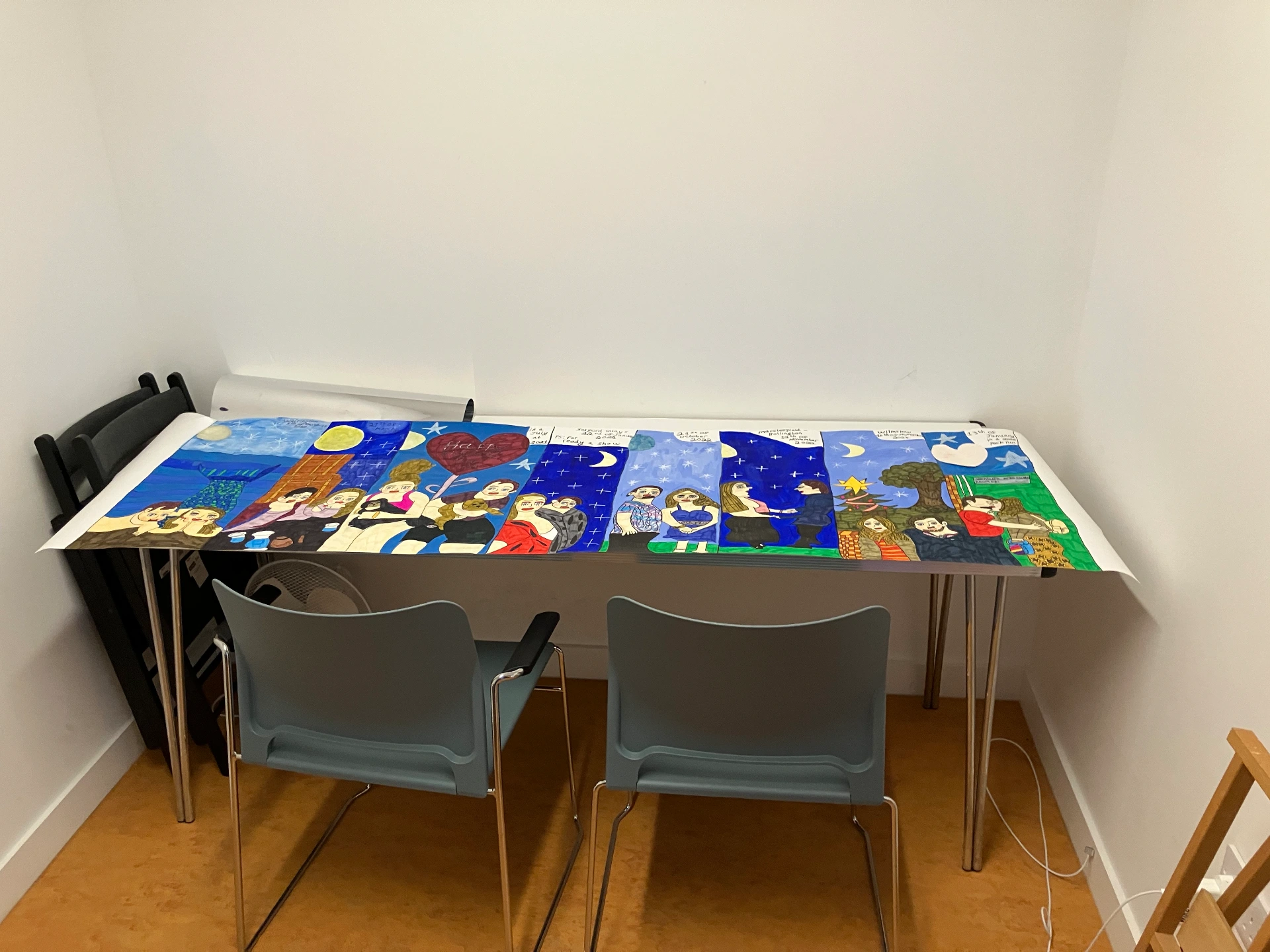 A long painted banner showing multiple figures against starry night skies is laid across a table in a small room.